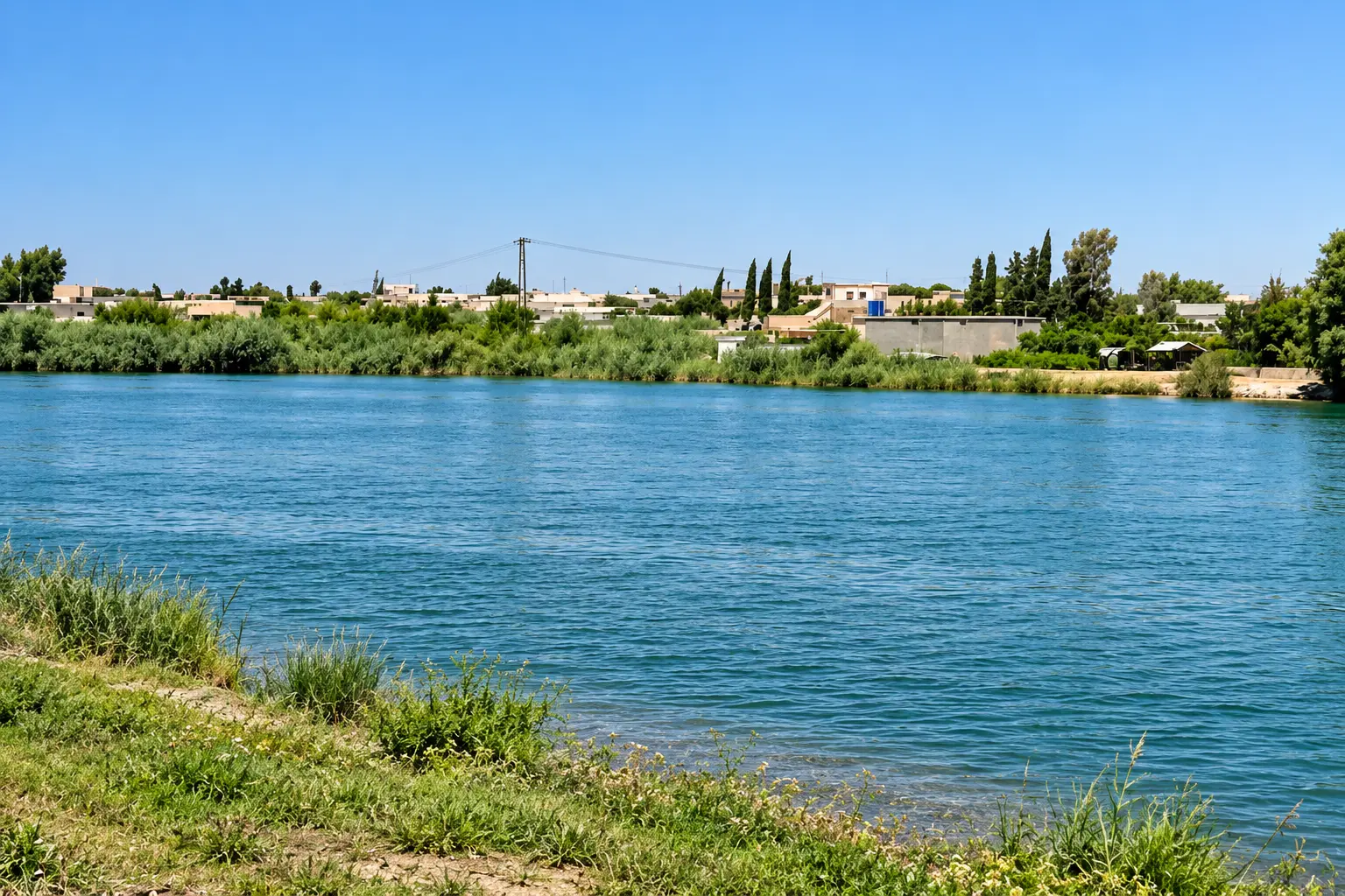 The Euphrates River with the opposite riverbank and green farmland in Raqqa